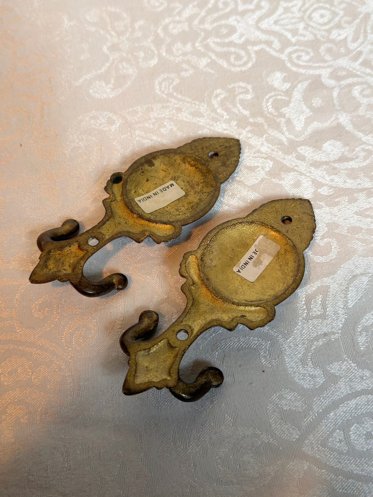 back of Pair of ornate brass floral wall hooks with made in India stickers on a white background