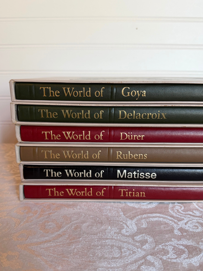 Stack of books titled 'The World of' with artists' names on a textured surface.