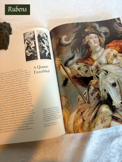 Open book with a painting of a queen on horseback and text, featuring the artist 'Rubens'.