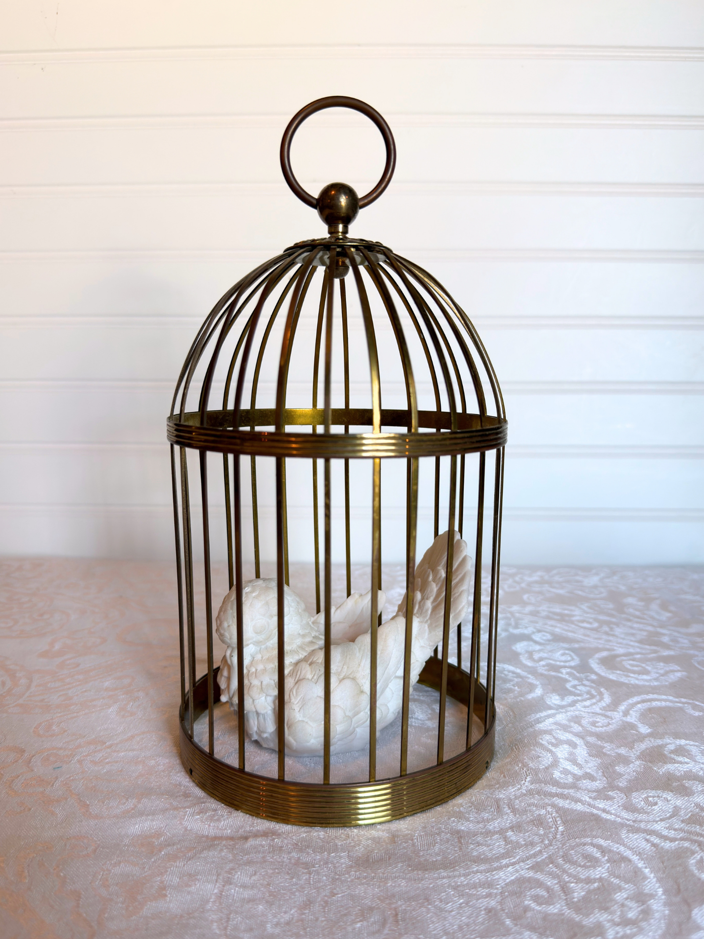 Decorative brass birdcage with a white decorative bird inside on a patterned surface.