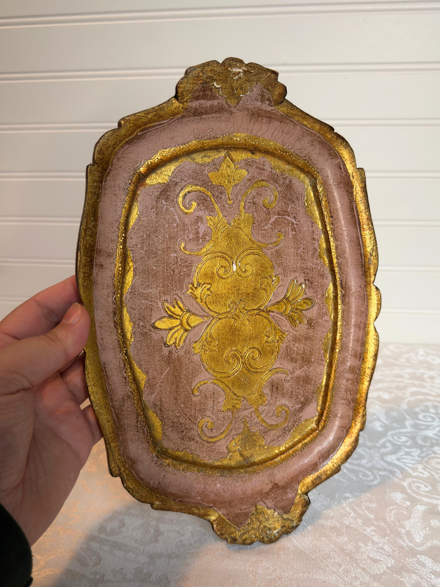 Decorative pink and gold wood tray held by a hand against a neutral background