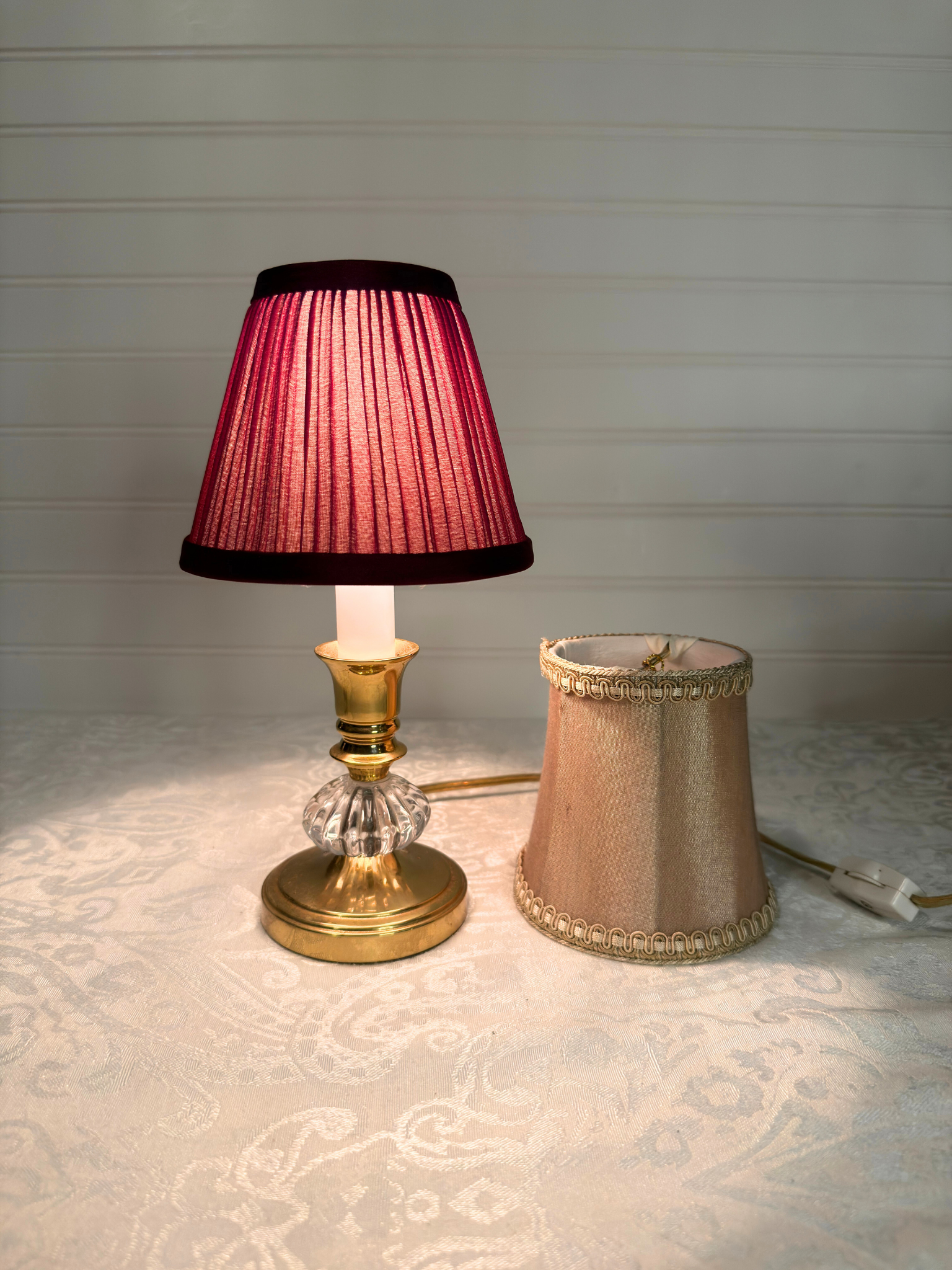 Table lamp with a burgundy pleated shade and champagne color  shade  on a textured surface.