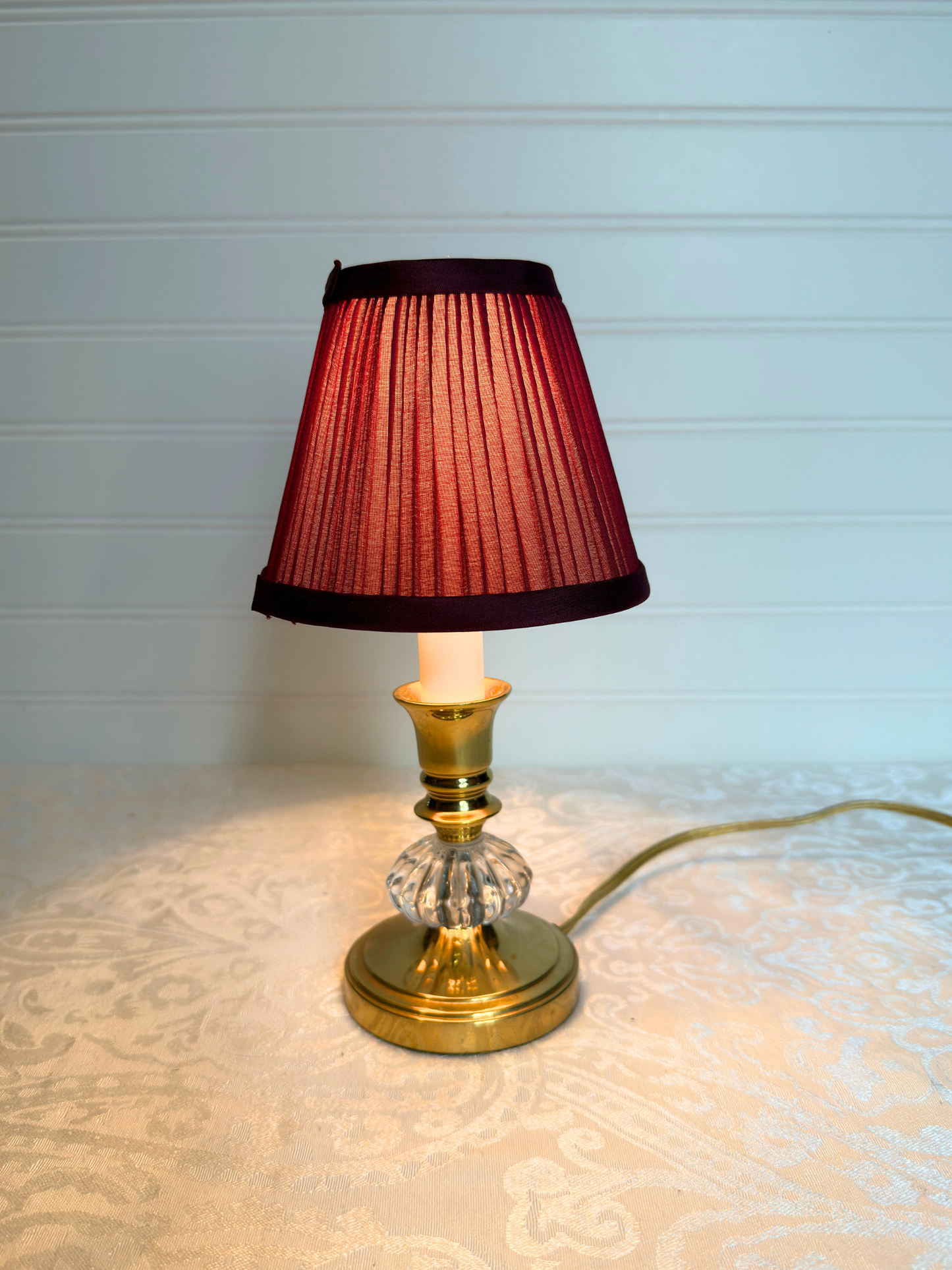 Small table lamp with a burgundy  pleated shade on a textured surface.
