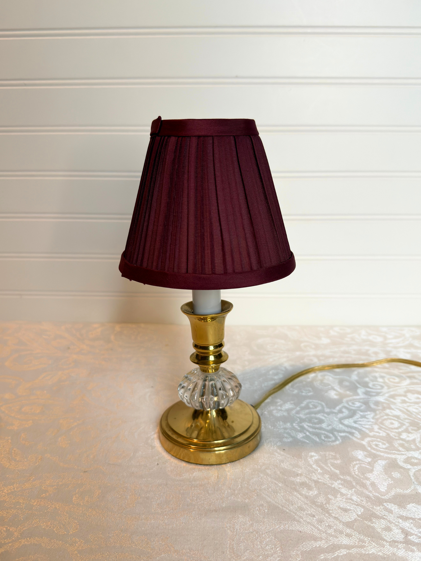 Table lamp with a burgundy shade and gold base on a textured surface.
