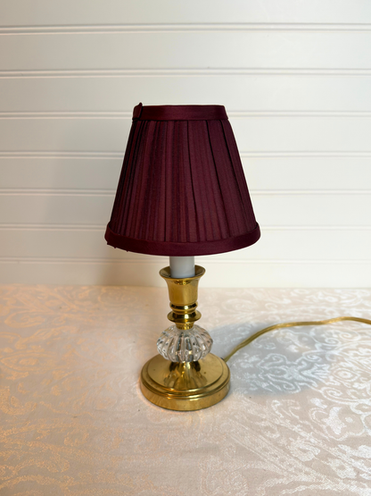Table lamp with a burgundy shade and gold base on a textured surface.