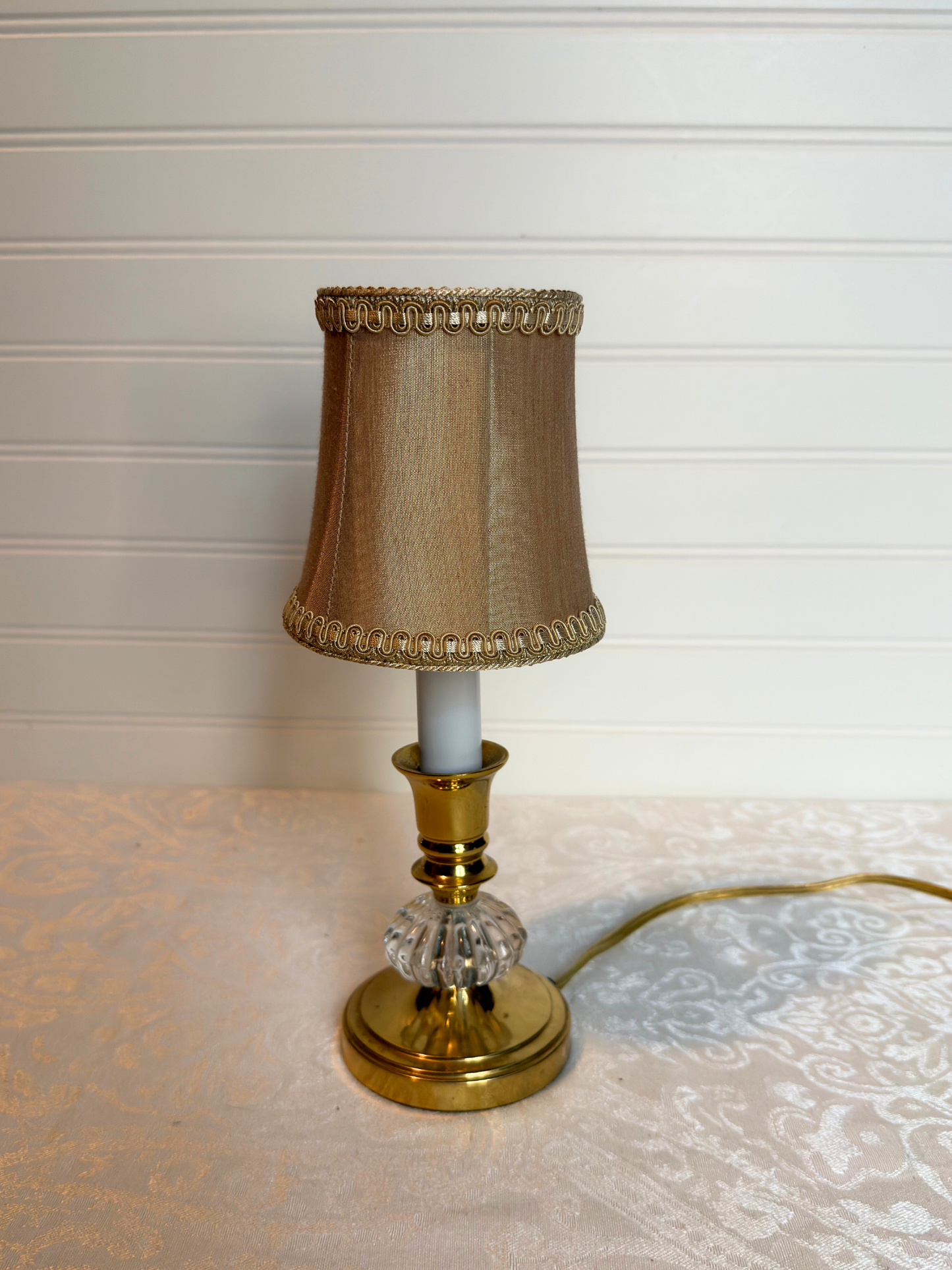 Small table lamp with a champagne base and decorative shade on a textured surface.