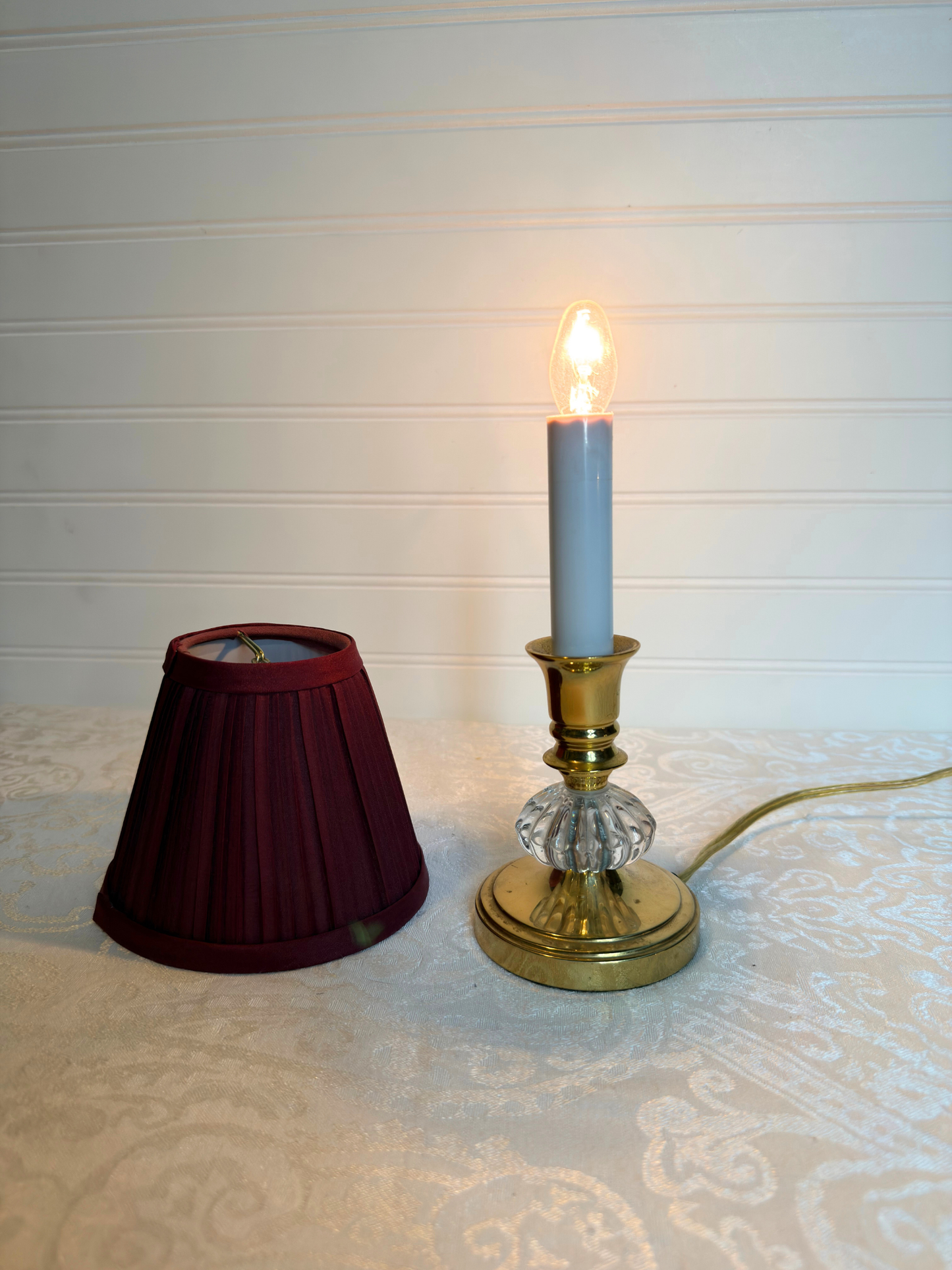Small lamp with a burgundy shade and clear base on a textured surface.
