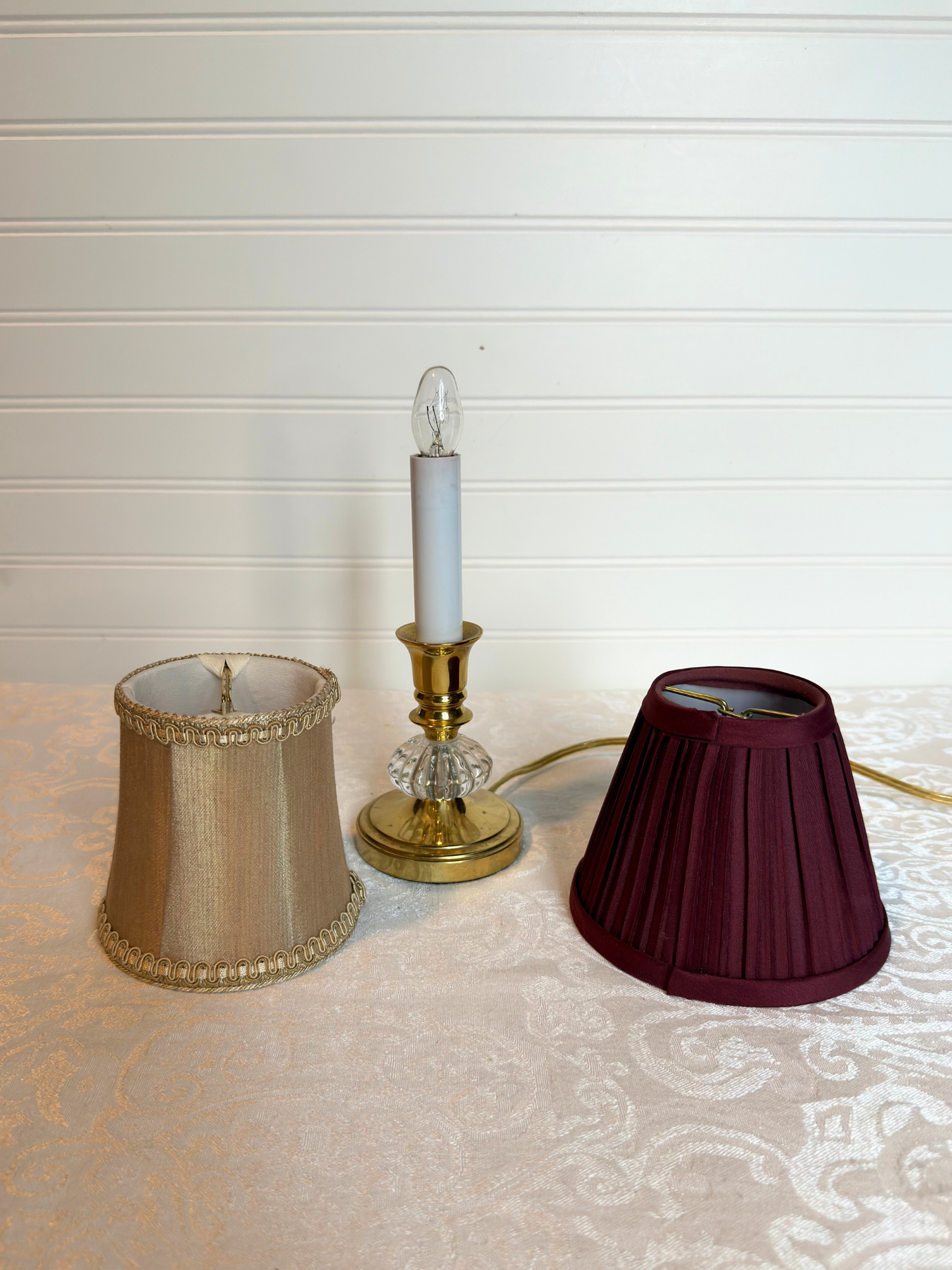 Gold lamp base with champagne shade on left and burgundy shade on right on a white background. 