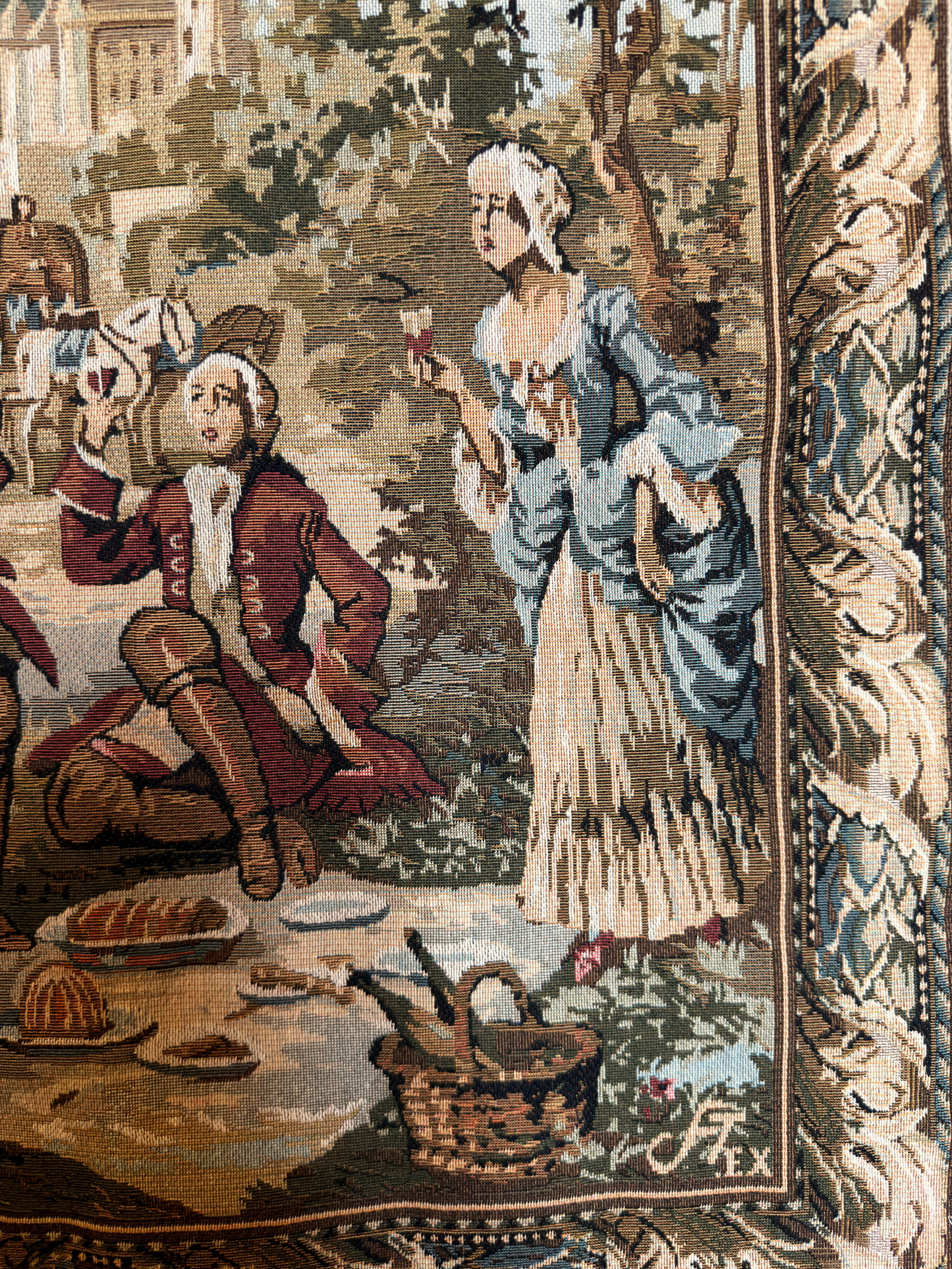 Tapestry depicting a classical scene with two figures at a table outdoors.
