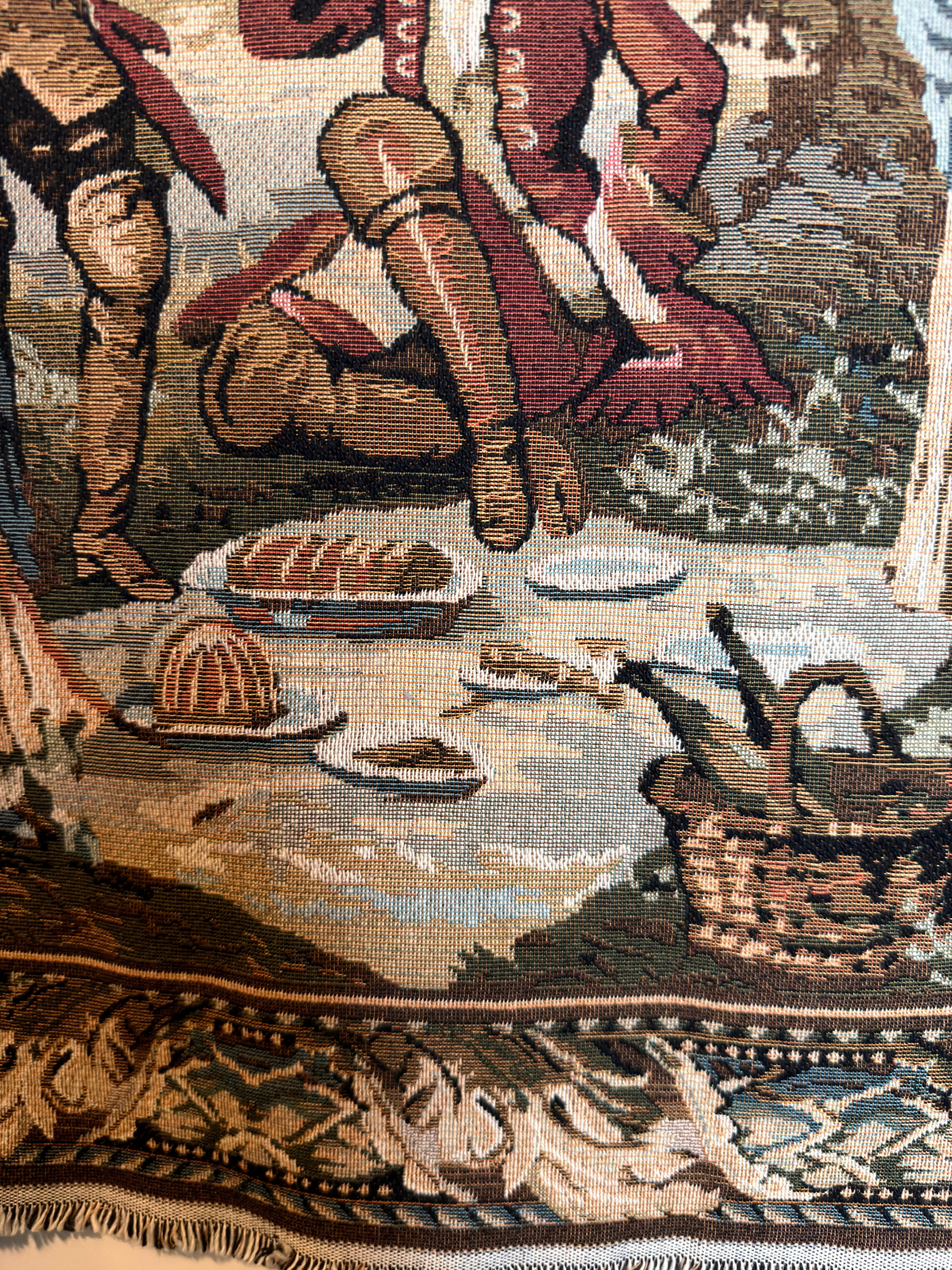 Close-up of a tapestry depicting a rustic scene with a person, food, and a basket.