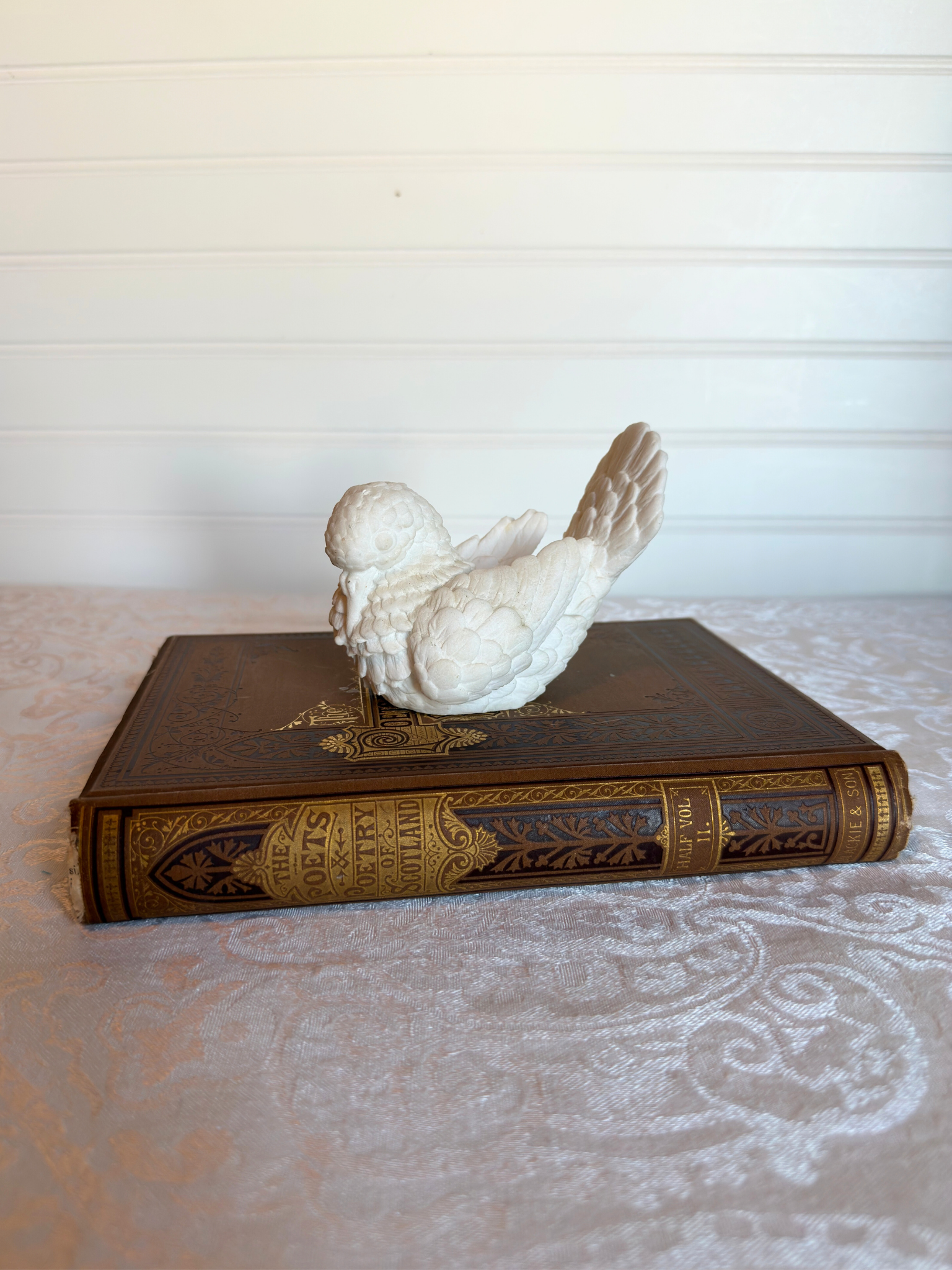Decorative white bird figurine on an ornate book with a neutral background