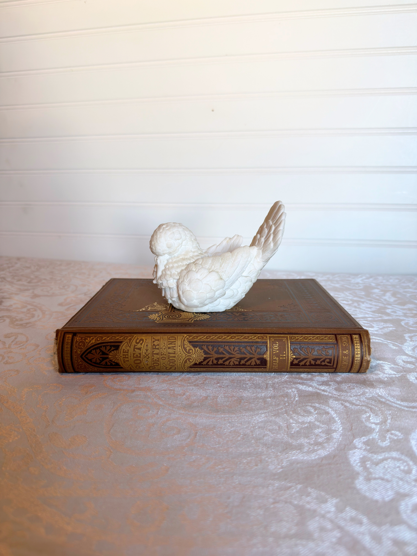 Decorative white bird figurine on a vintage book with a white lace tablecloth and wooden surface background.