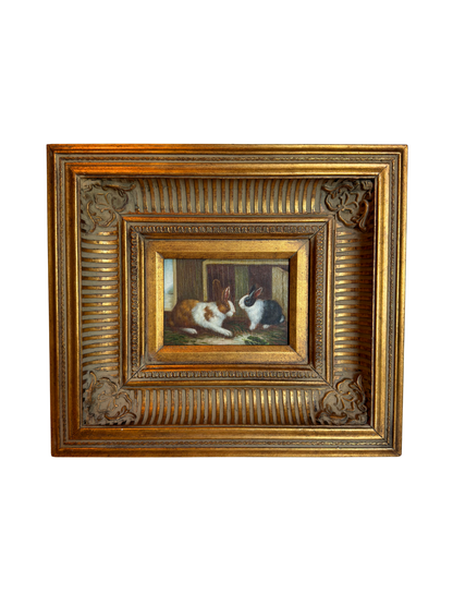 Framed painting of two bunnies in a decorative gold frame on a white background