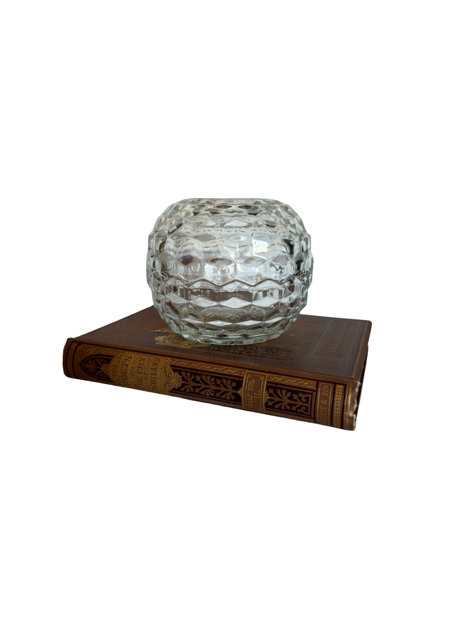 Clear glass candle holder on a decorative book with a white background