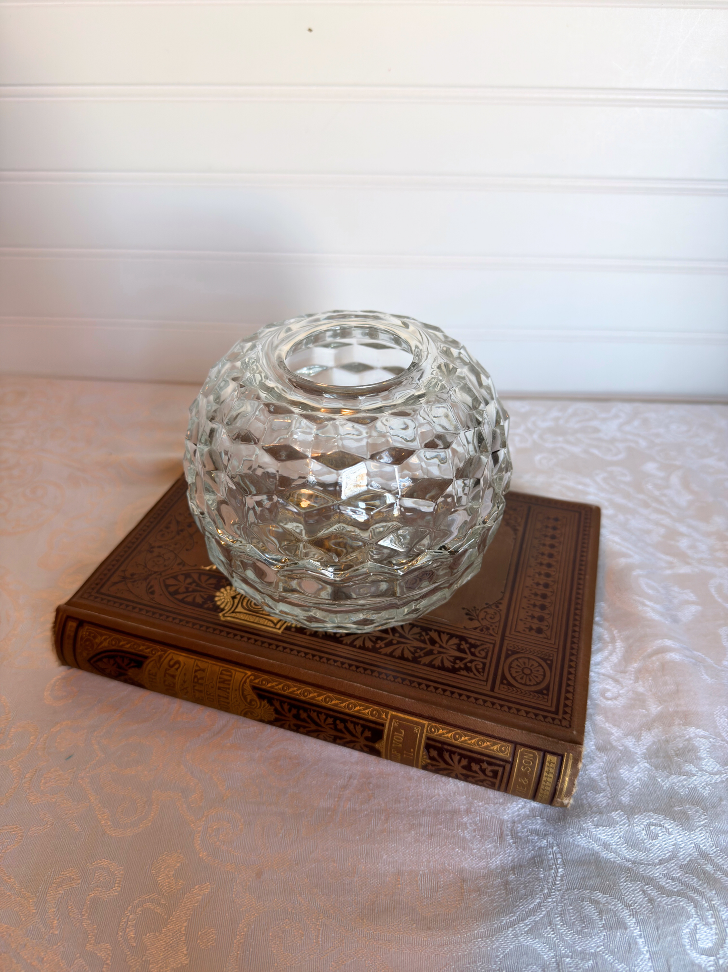 Clear glass candle holder on an ornate book with a white background