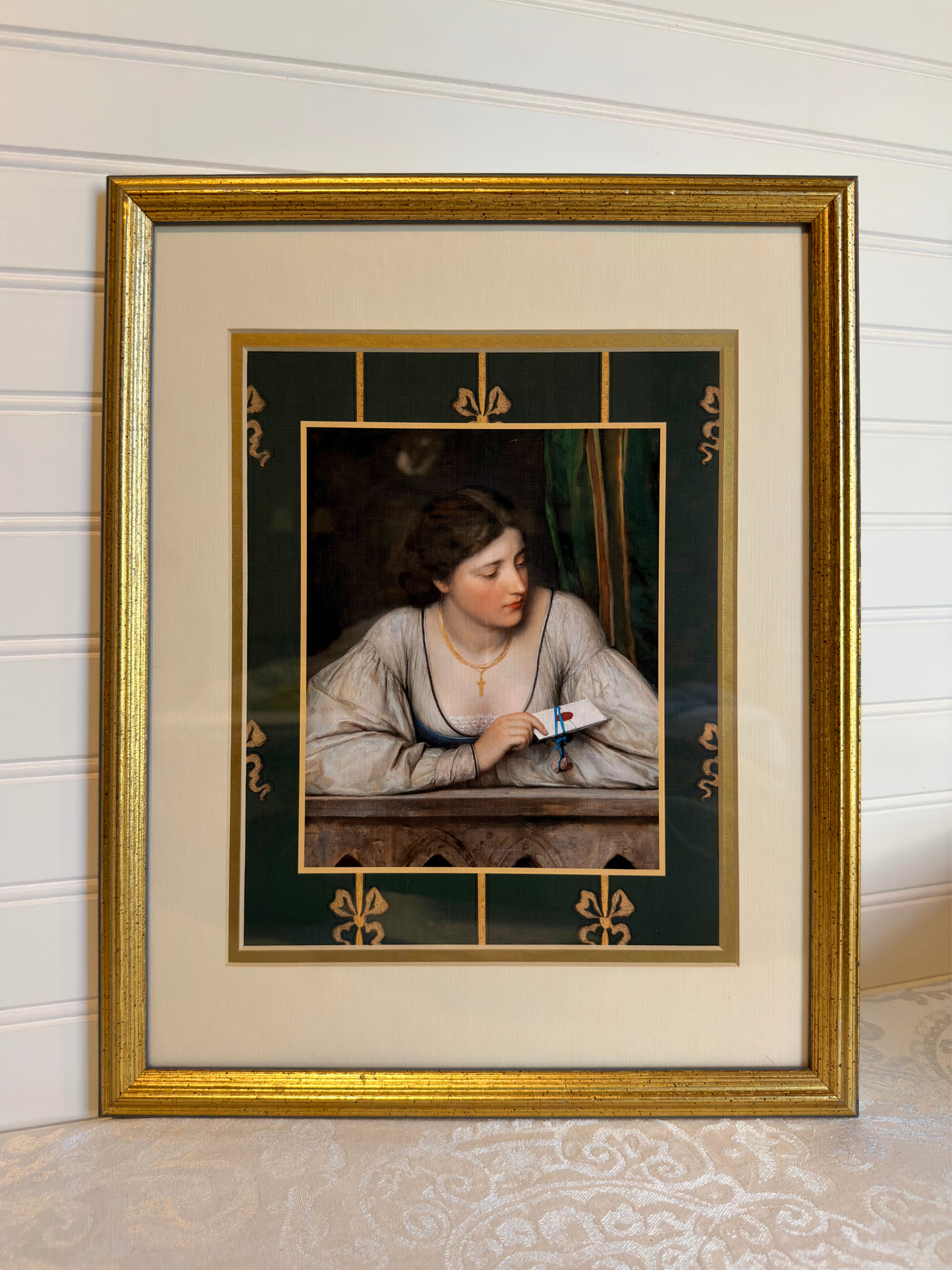 Framed artwork of a woman holding a letter with decorative gold frame and green border with bows.