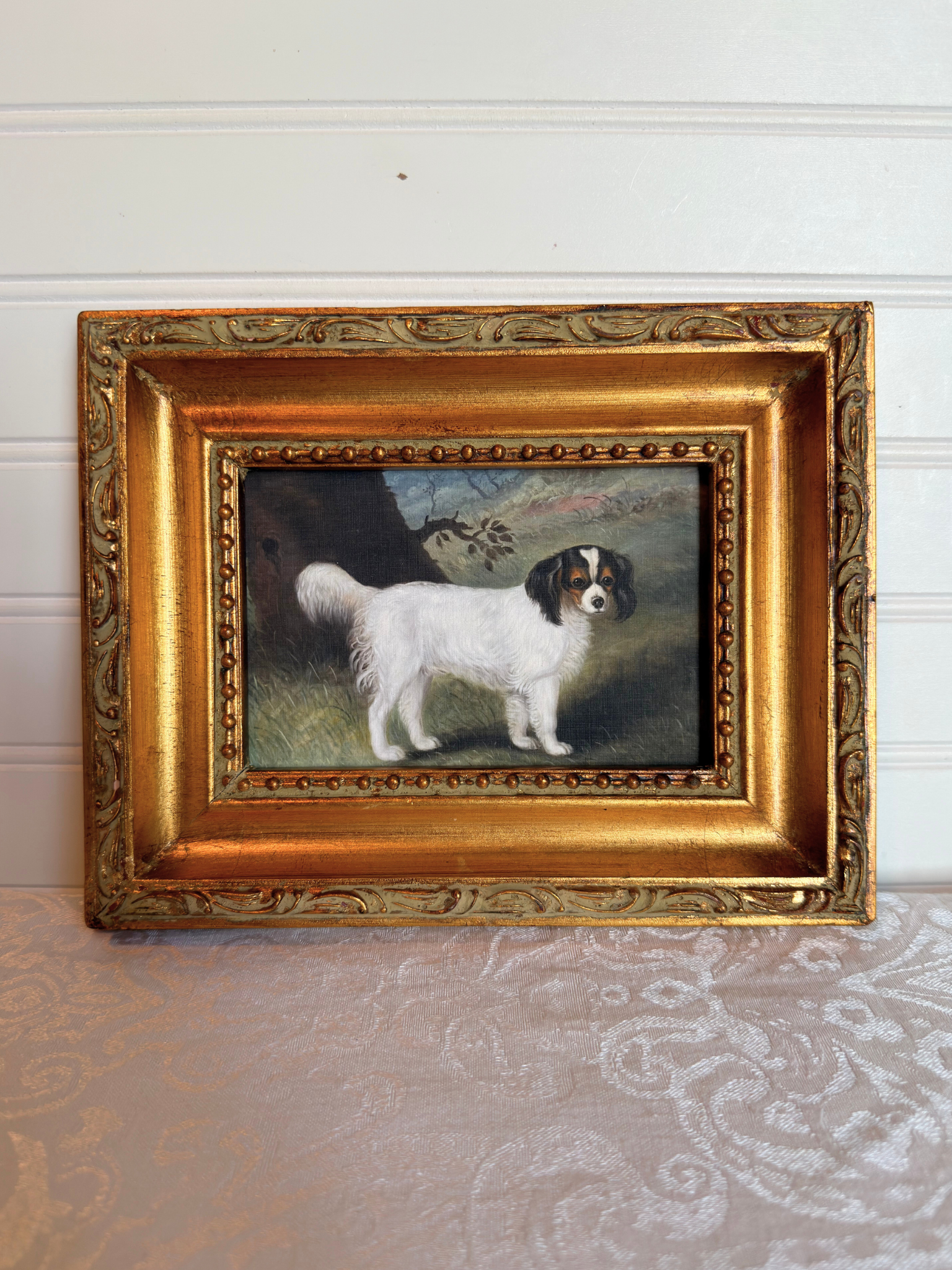 Small print of a white and black King Charles spaniel in a decorative gold frame on a white background