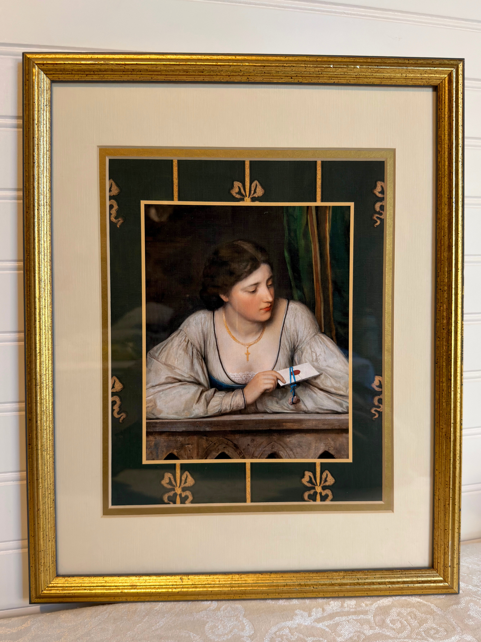 Framed artwork of a woman holding a letter with decorative gold frame and green border with bows.