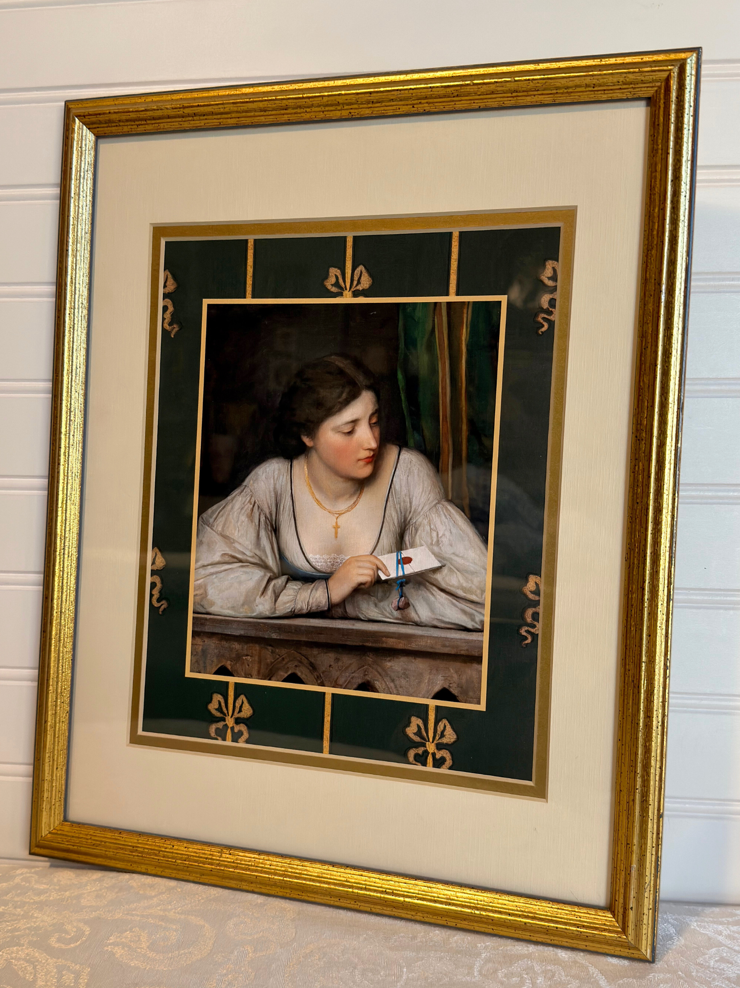 Framed artwork of a woman holding a letter with decorative gold frame and green border with bows.