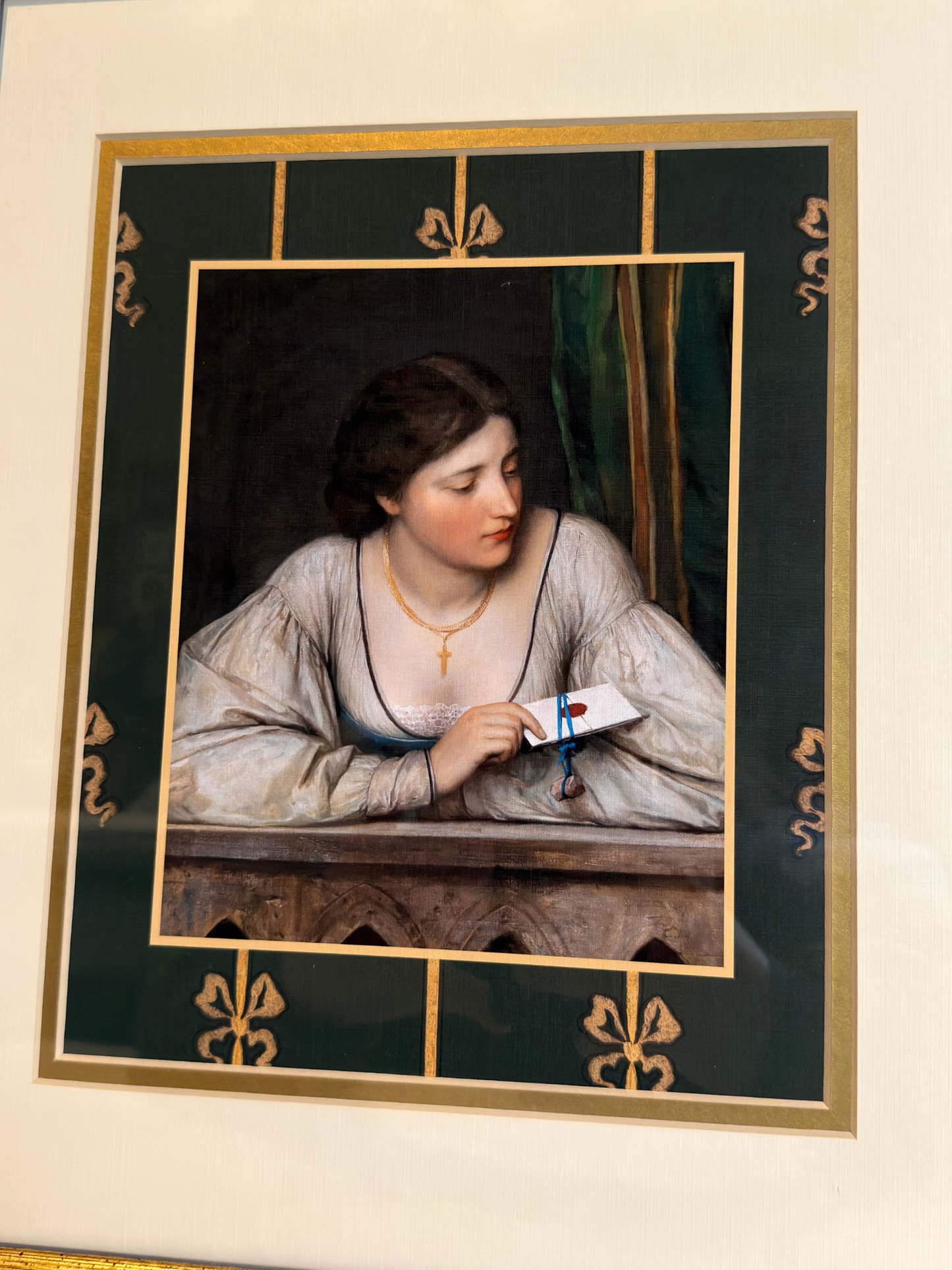 Framed artwork of a woman holding a letter with decorative gold frame and green border with bows.