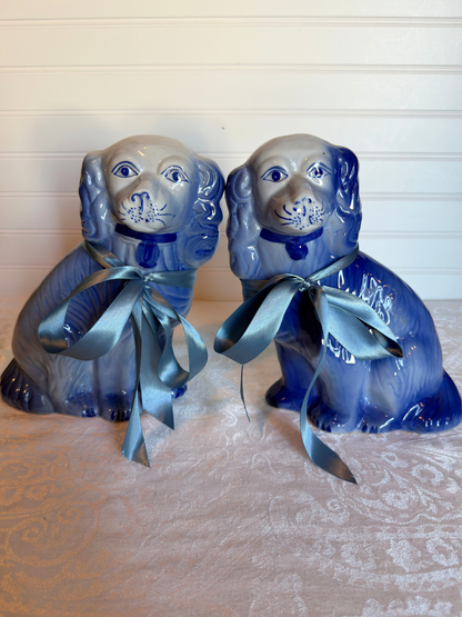 Two blue Staffordshire dogs with blue ribbons on a textured white background