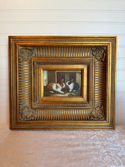 Framed painting of two bunnies in a decorative gold frame on a white background