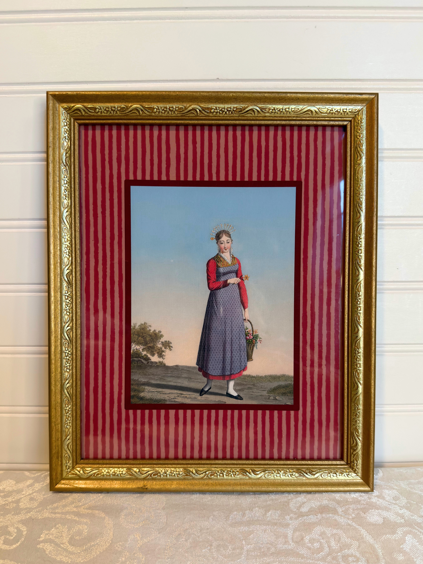 Framed artwork of a woman in a dress holding a basket on a red striped background