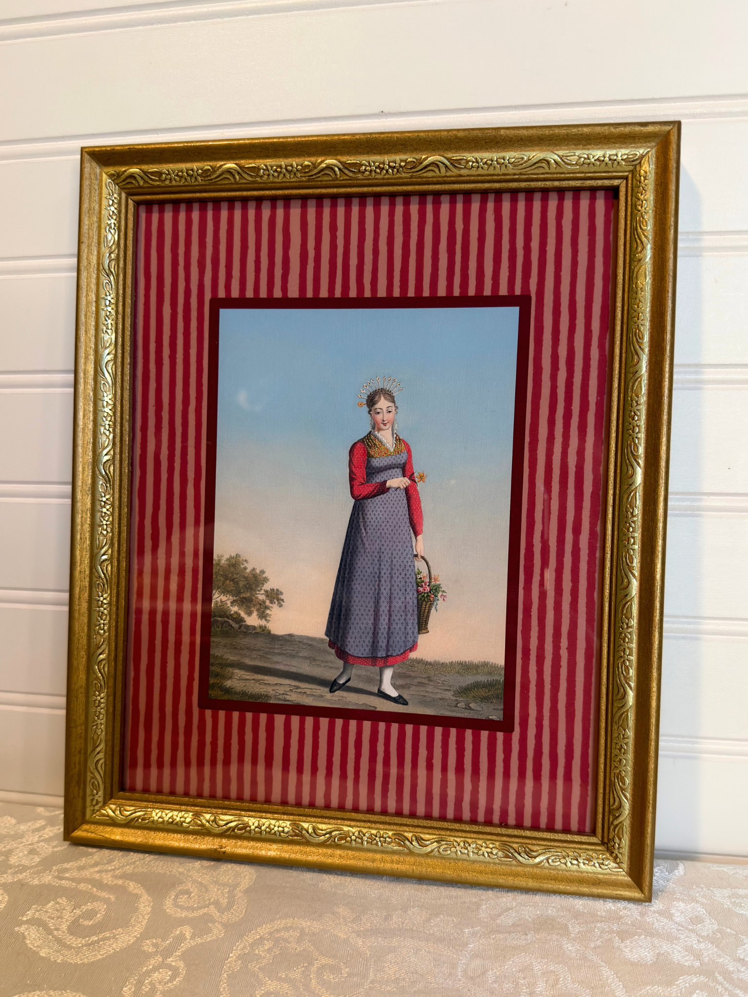 Framed artwork of a woman in a dress holding a basket on a red striped background
