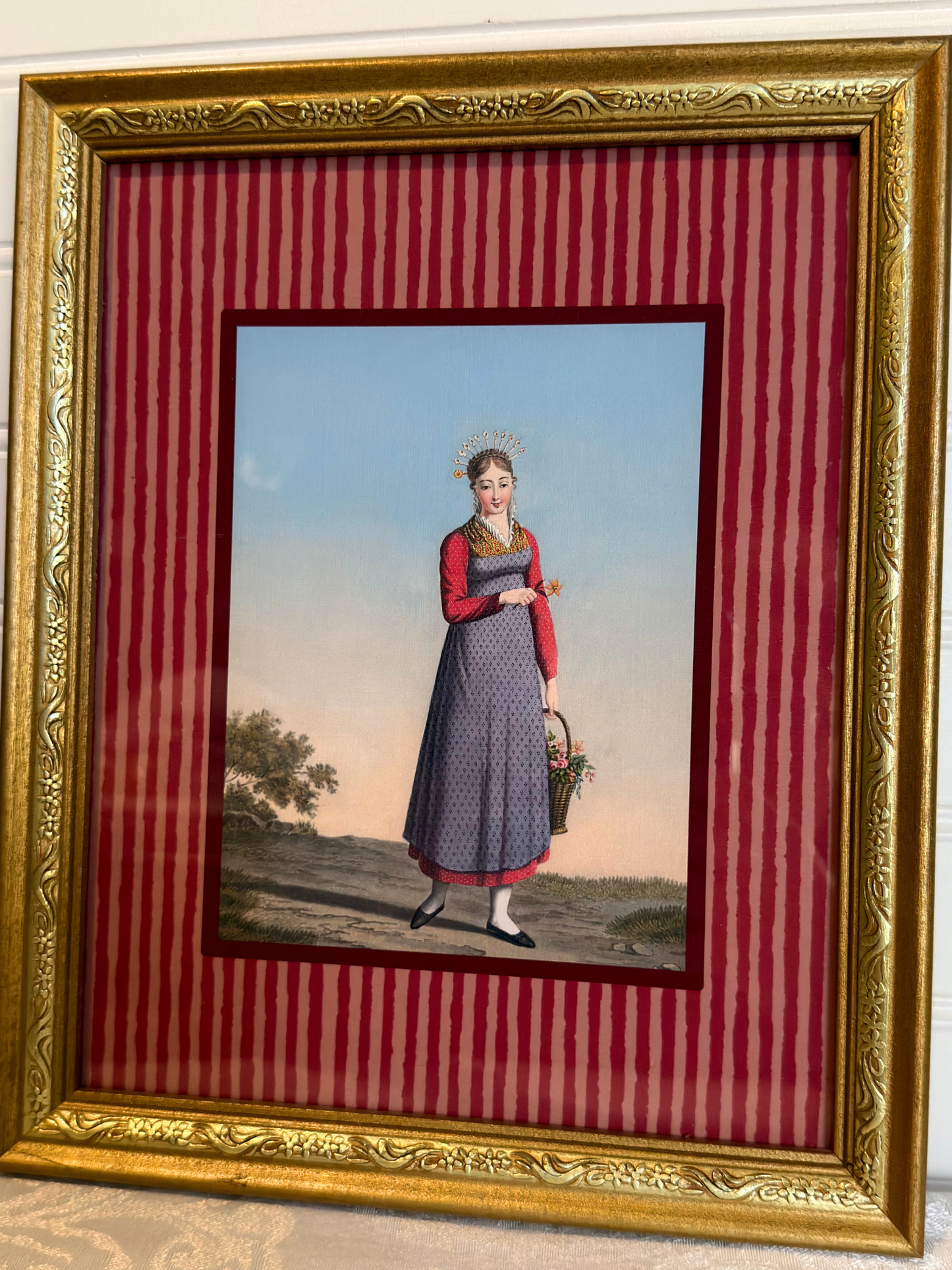 Framed artwork of a woman in a dress holding a basket on a red striped background