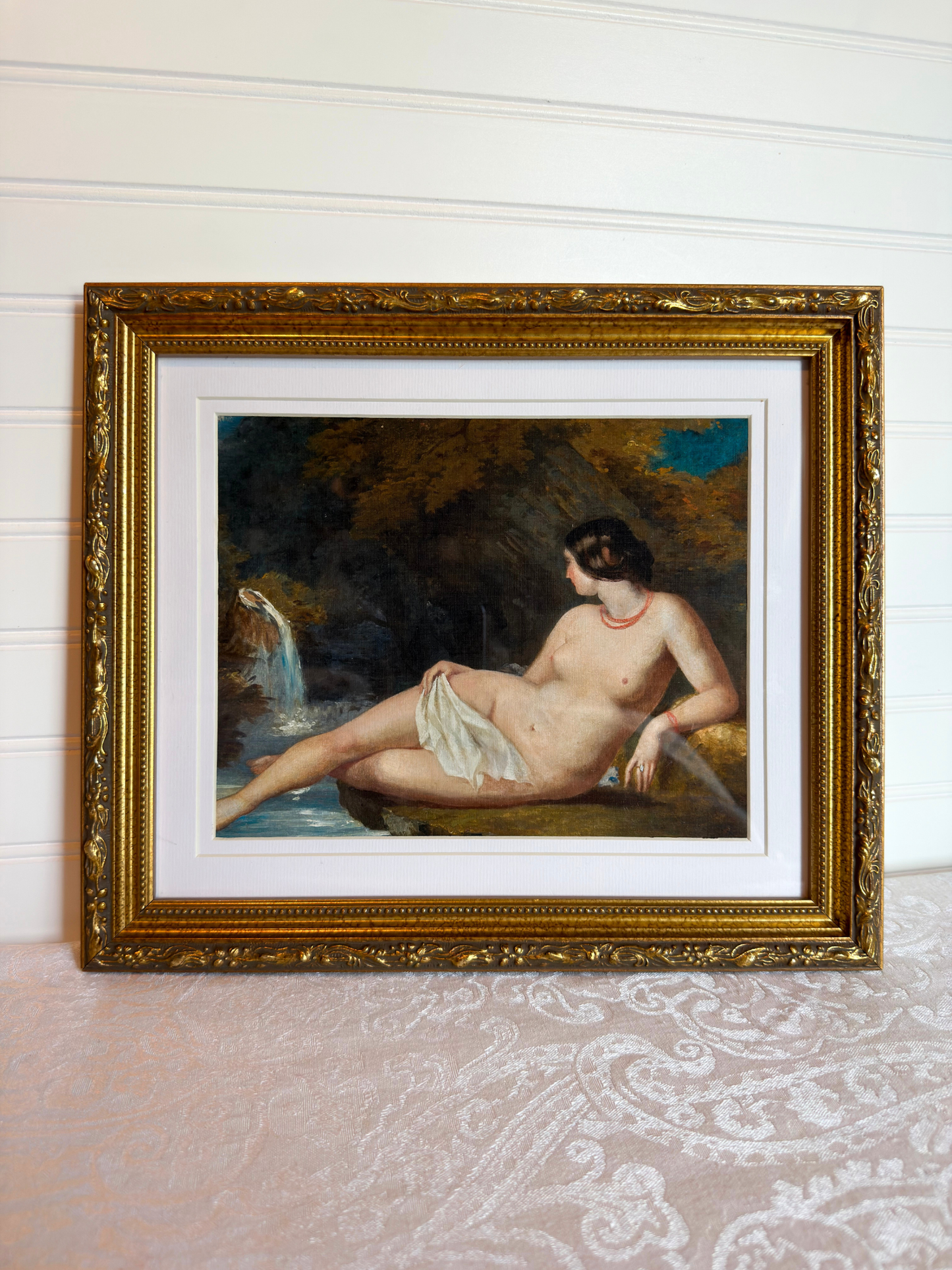 Framed print of a nude woman by a waterfall with a gold frame.