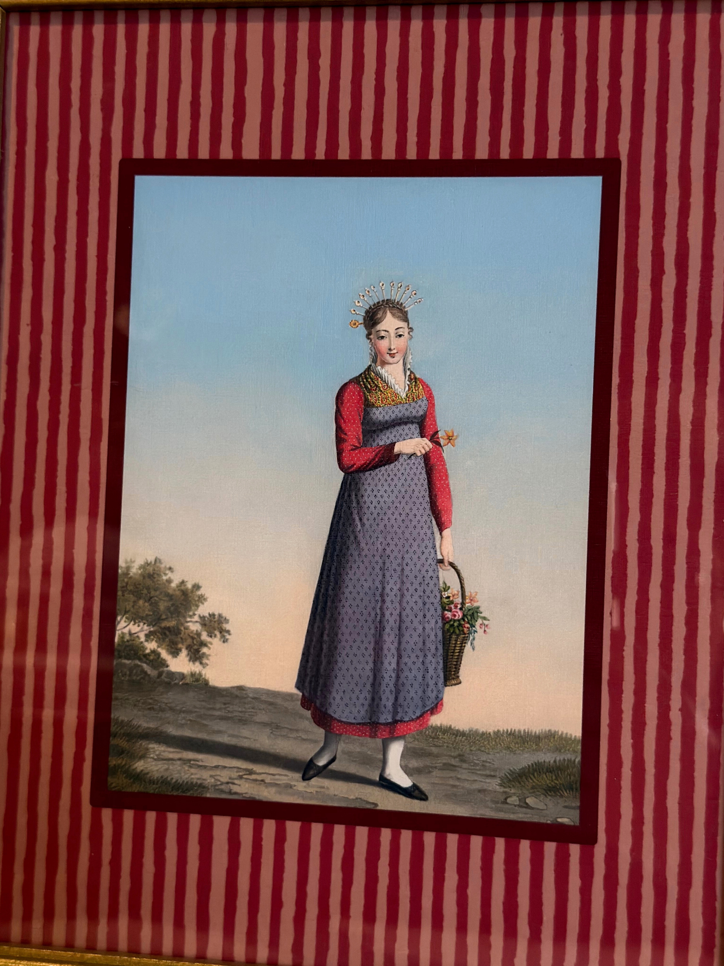 Framed artwork of a woman in a dress holding a basket on a red striped background
