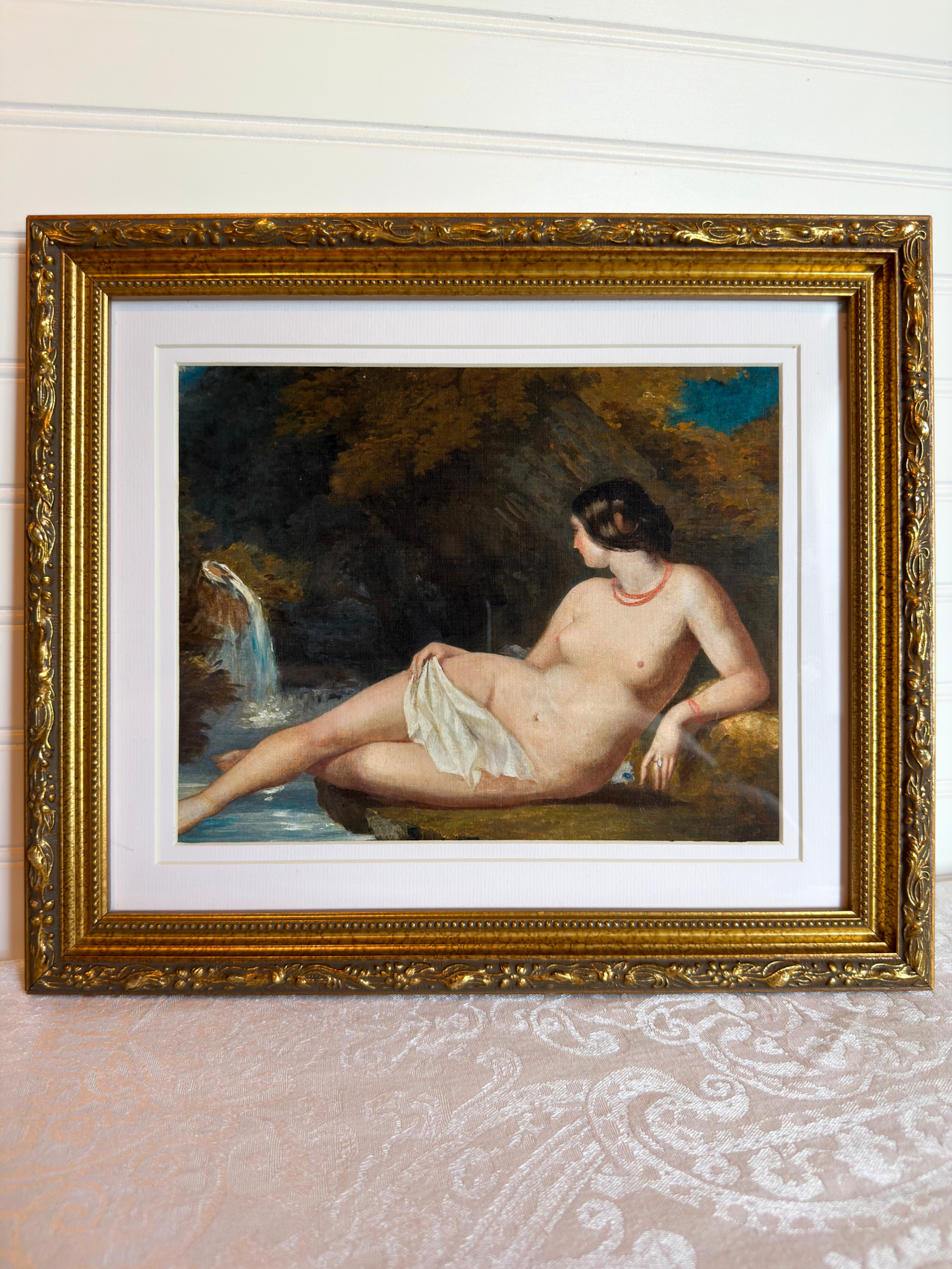 Framed print of a nude woman by a waterfall with a gold frame.
