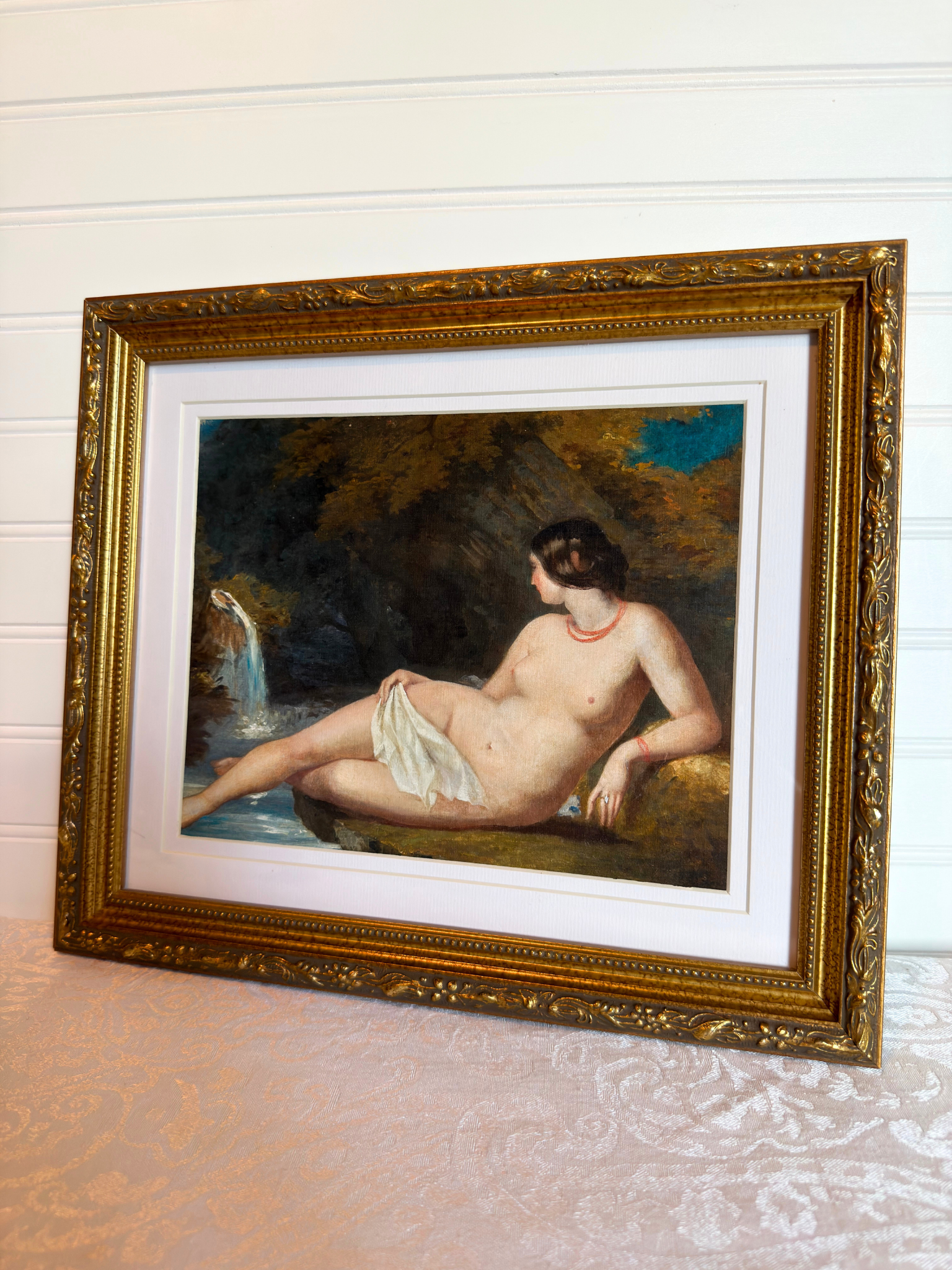 Framed print of a nude woman by a waterfall with a gold frame.