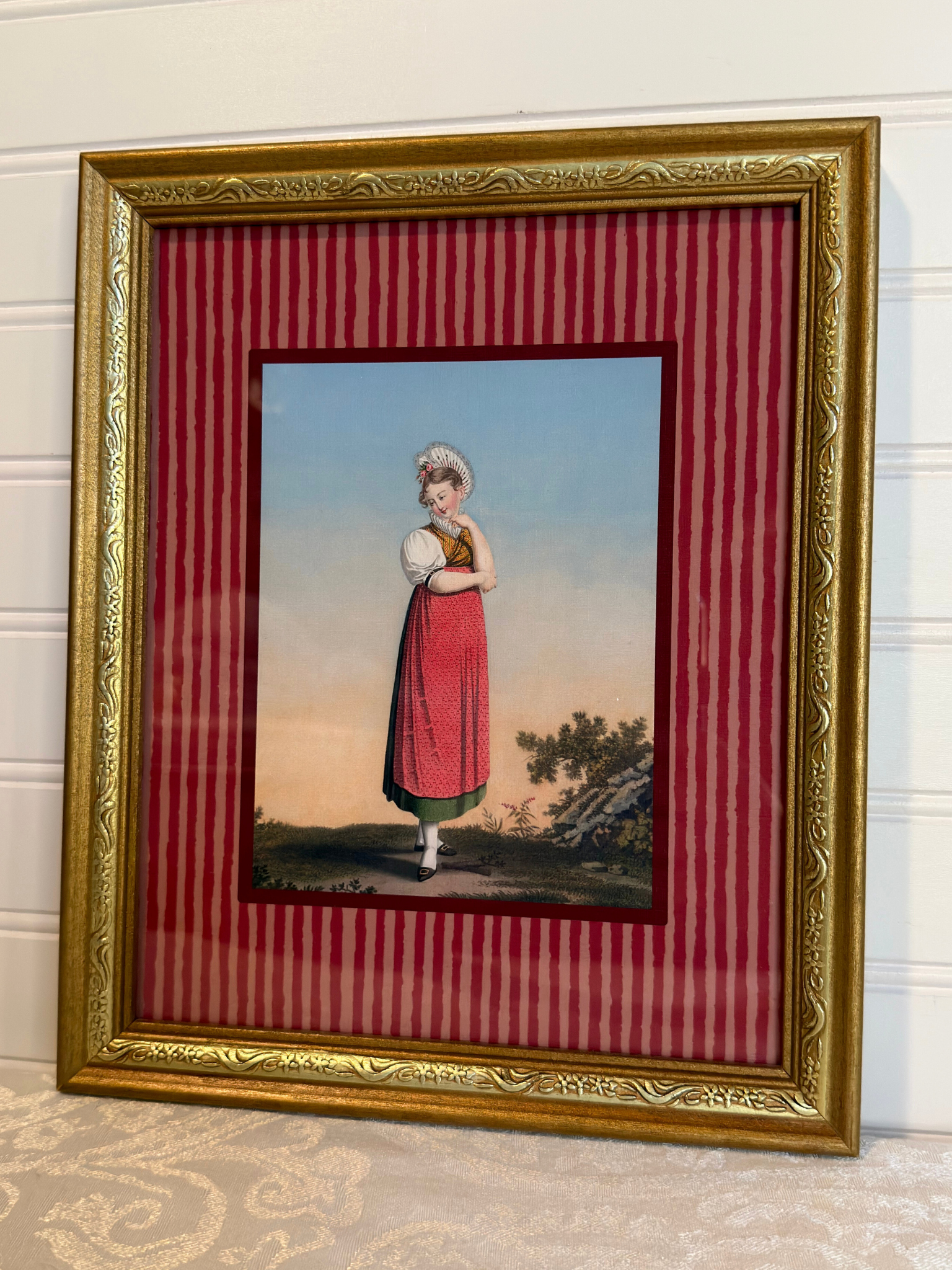 Framed artwork of a woman in a red dress, with a gold frame and red striped inner lining.