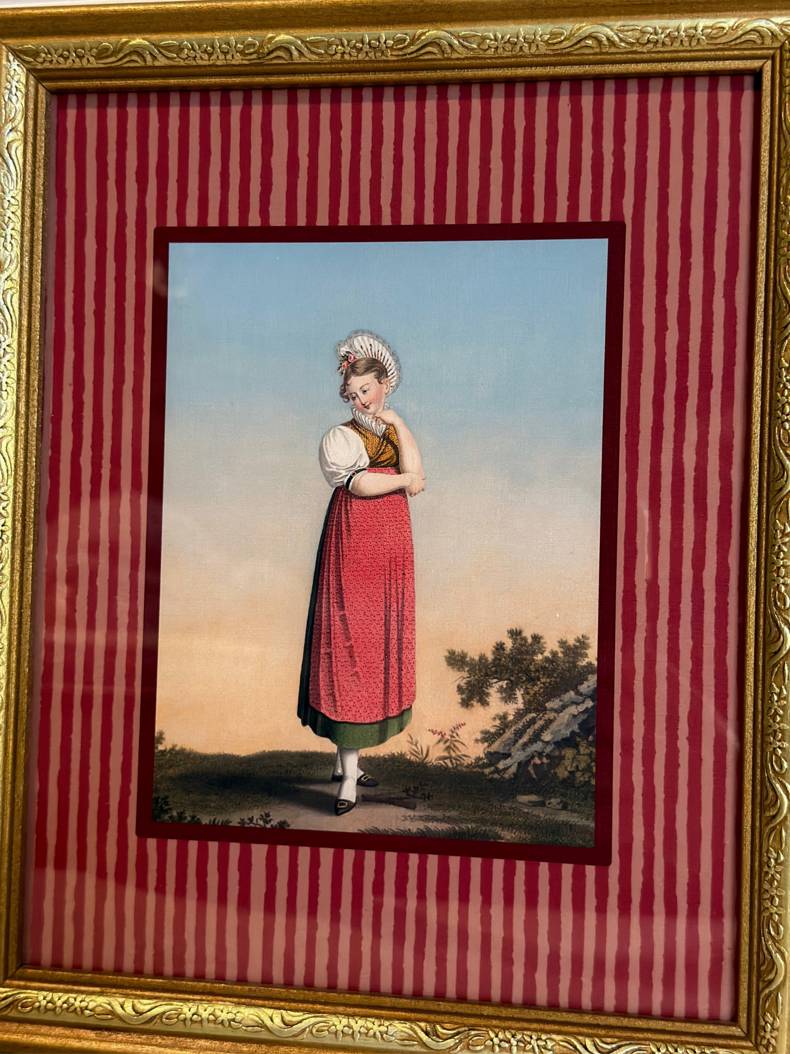 Framed artwork of a woman in a red dress, with a gold frame and red striped inner lining.