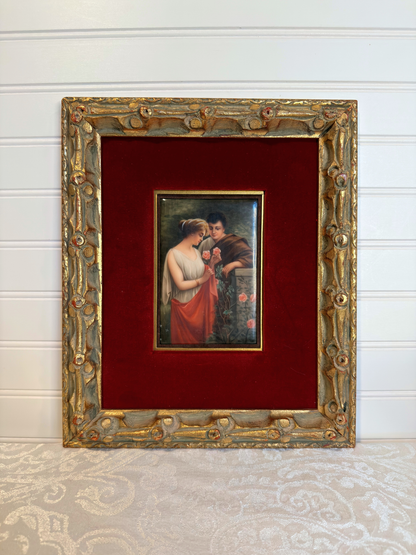 Small painting of couple with roses  within a decorative gold frame on a red background