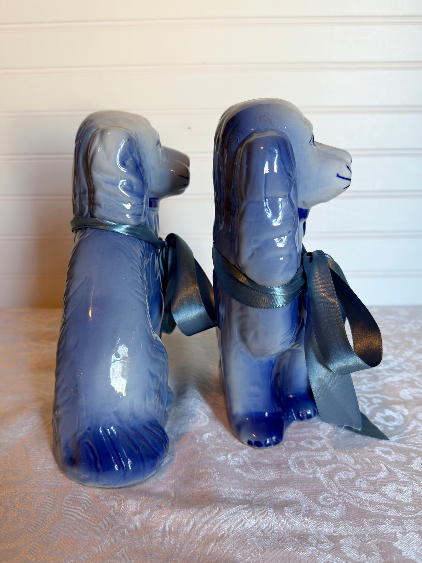 Two blue Staffordshire dogs with blue ribbons on a textured white background