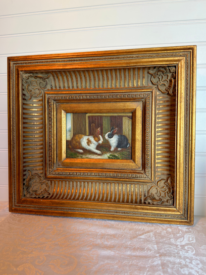 Decorative painting of two rabbits in a ornate gold frame on a textured surface.