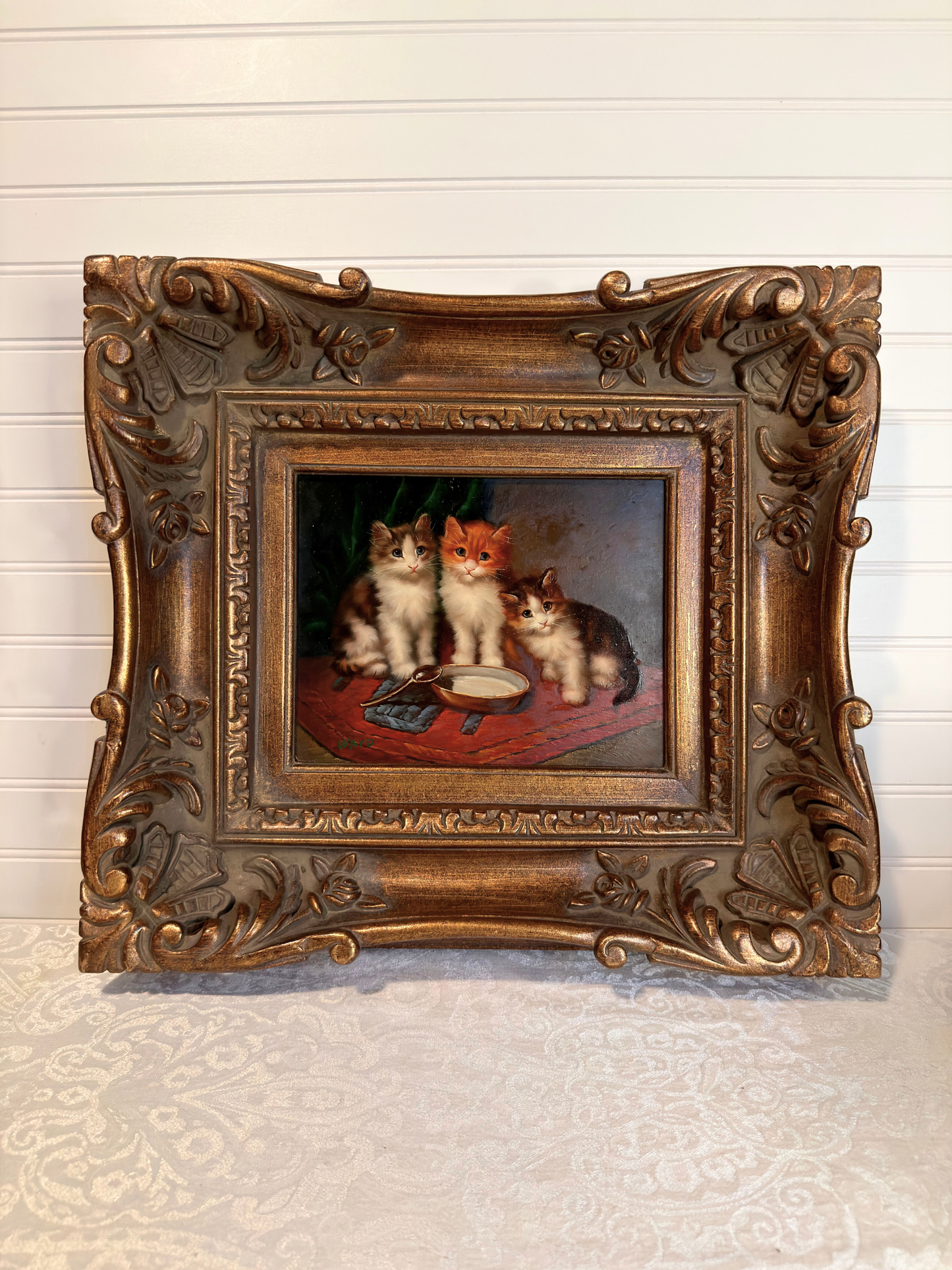 Decorative painting of three cats in a ornate gold frame on a textured wall.