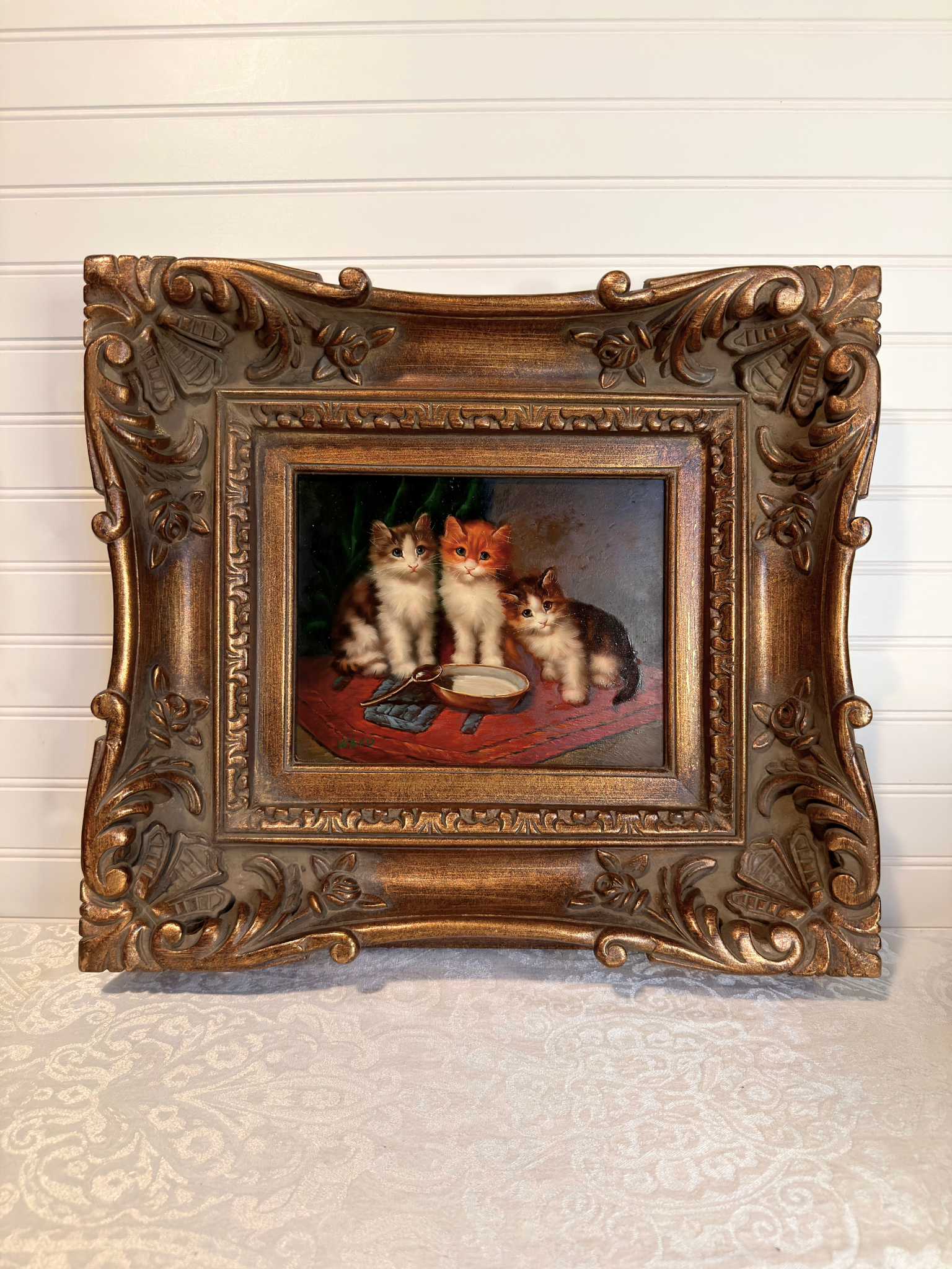 Decorative painting of three cats in a ornate gold frame on a textured wall.