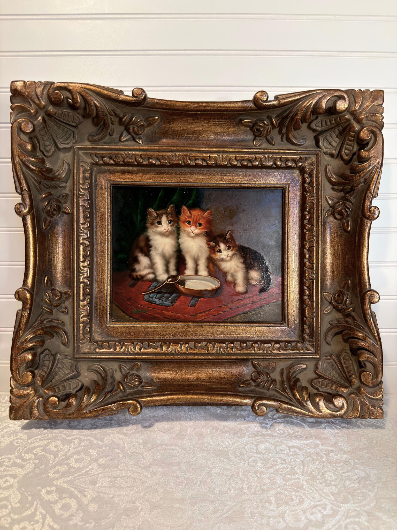 Decorative painting of three cats in a ornate bronze frame on a textured wall.