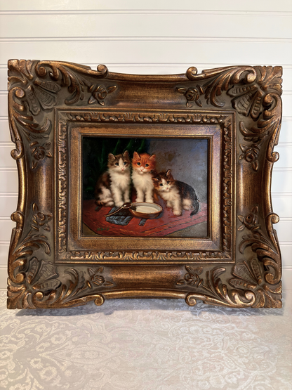 Decorative painting of three cats in a ornate bronze frame on a textured wall.