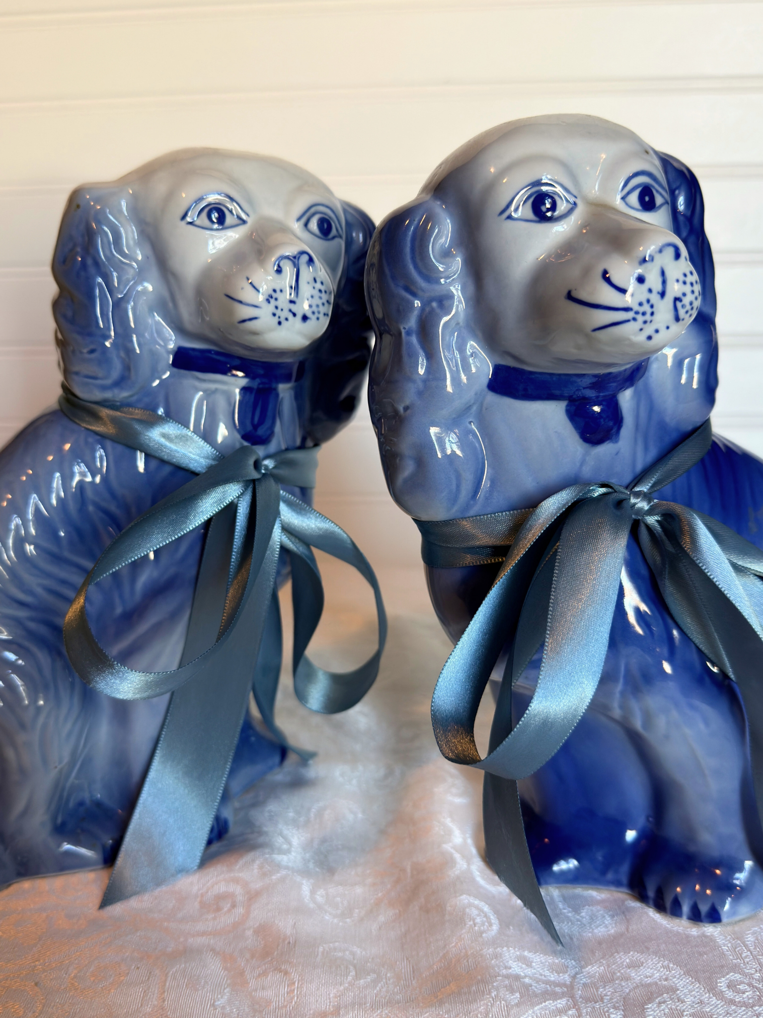 Two blue Staffordshire dogs with blue ribbons on a textured white background