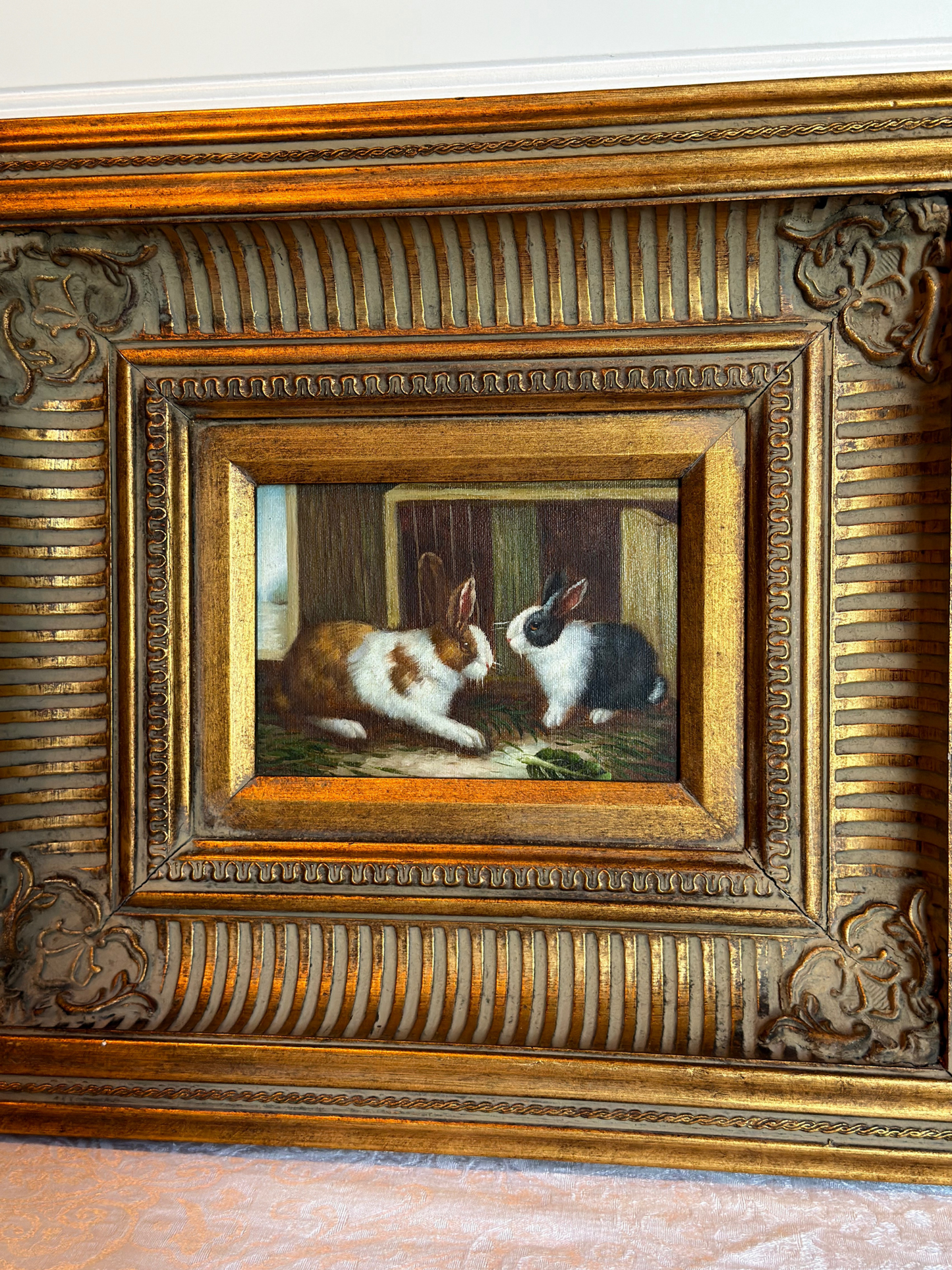 Framed painting of two bunnies in a decorative gold frame on a white background