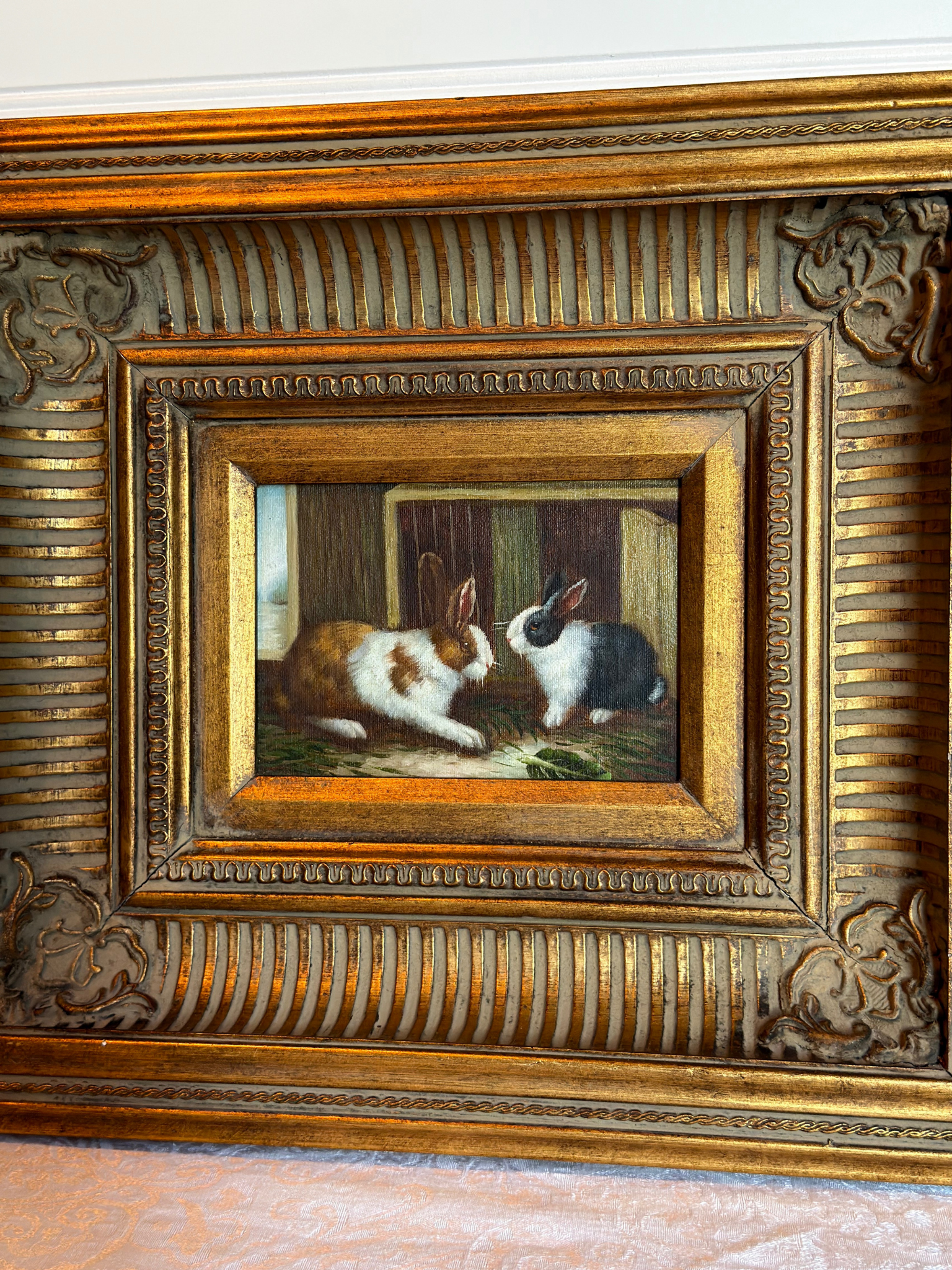 Framed painting of two bunnies in a decorative gold frame on a white background