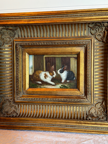 Framed painting of two bunnies in a decorative gold frame on a white background