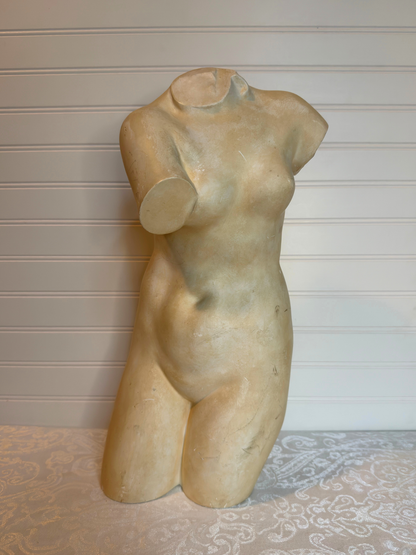 sculpture of a female torso on a textured surface with a neutral background