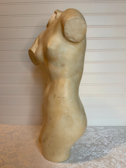 Statue of a nude female figure on a textured surface with a neutral background
