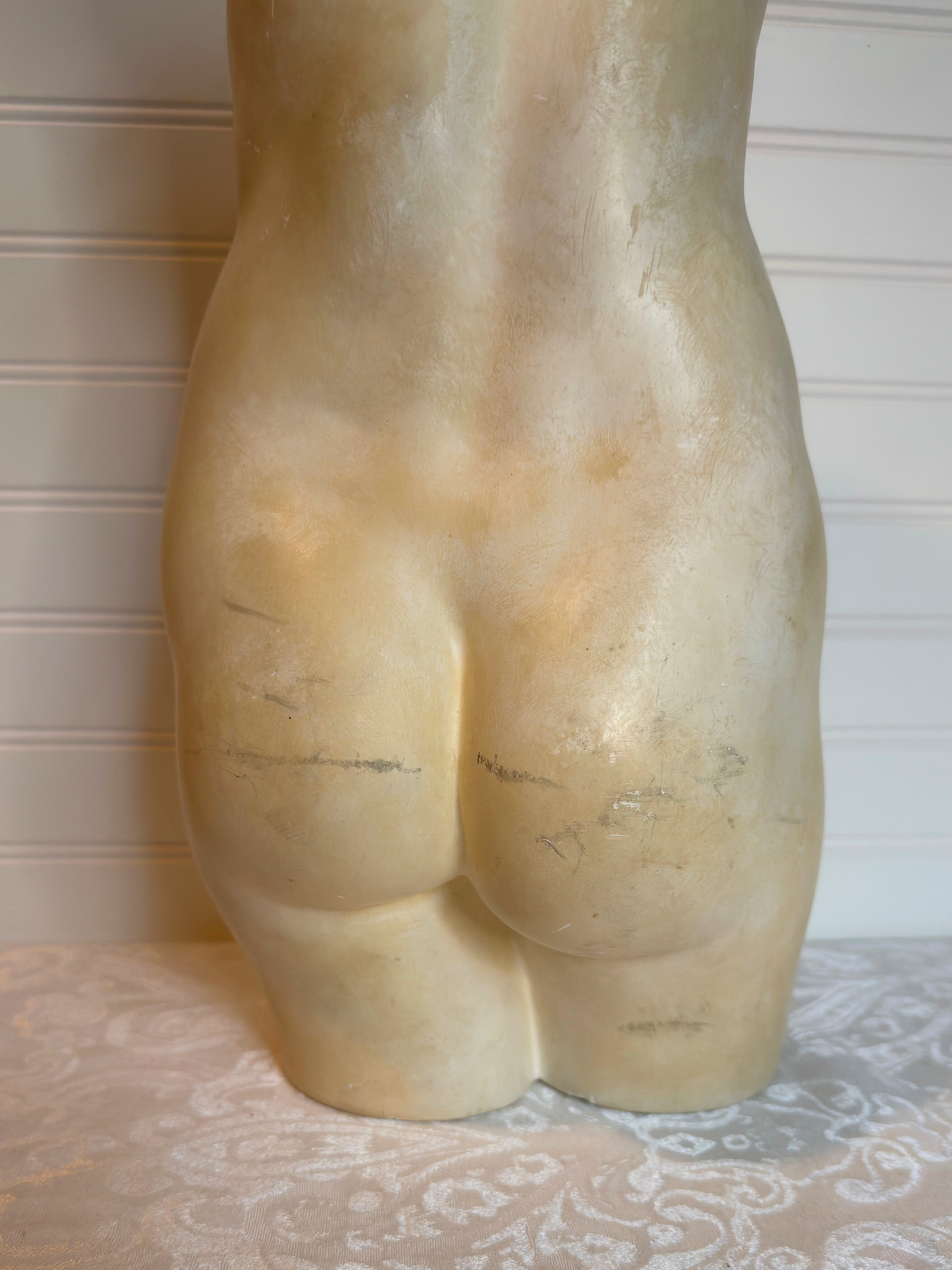 bottom back of sculpture of a torso on a textured surface with a neutral background