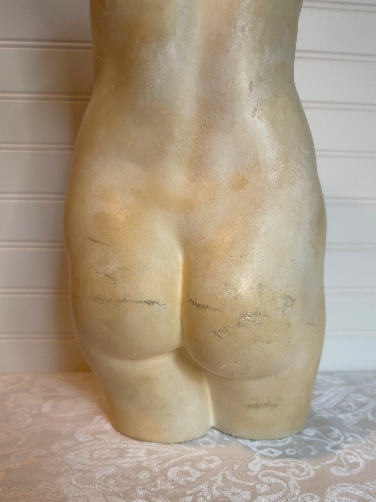 bottom back of sculpture of a torso on a textured surface with a neutral background